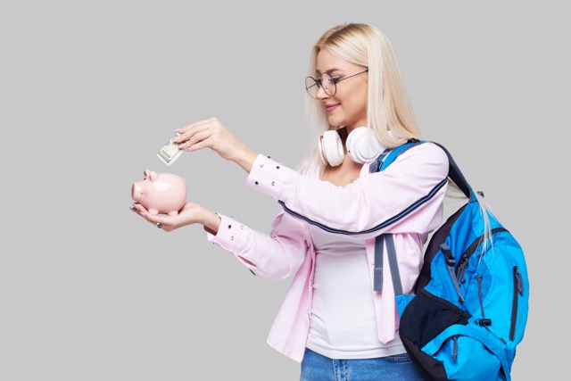 Cost of college education. Female student  puts cash in the piggy bank. The girl saves money for training in high school .Neutral grey background. Space for text